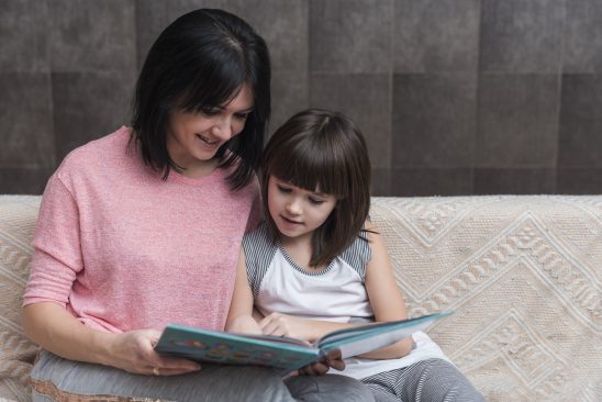 Ibu mendampingi anak belajar sambil memberikan dukungan emosional dan membaca buku bersama.
