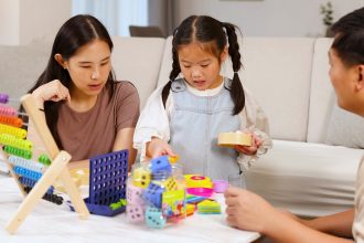 Anak mengelompokkan balok berdasarkan warna dan bentuk saat bermain bersama ibu di rumah.