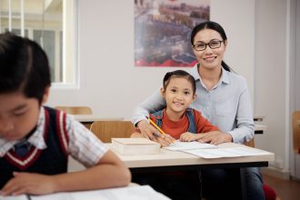 Guru membantu siswa mempersiapkan pelajaran sambil melatih kemandirian saat hari pertama sekolah.