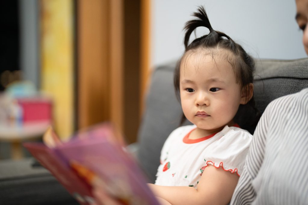 Stimulasi bahasa ekspresif melalui pilihan benda, bermain, dan membaca buku.