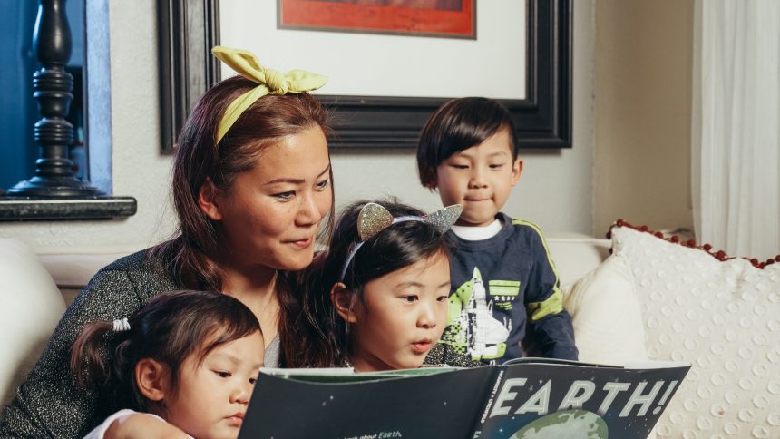 Ibu membaca buku interaktif bersama anak sambil menunjuk gambar